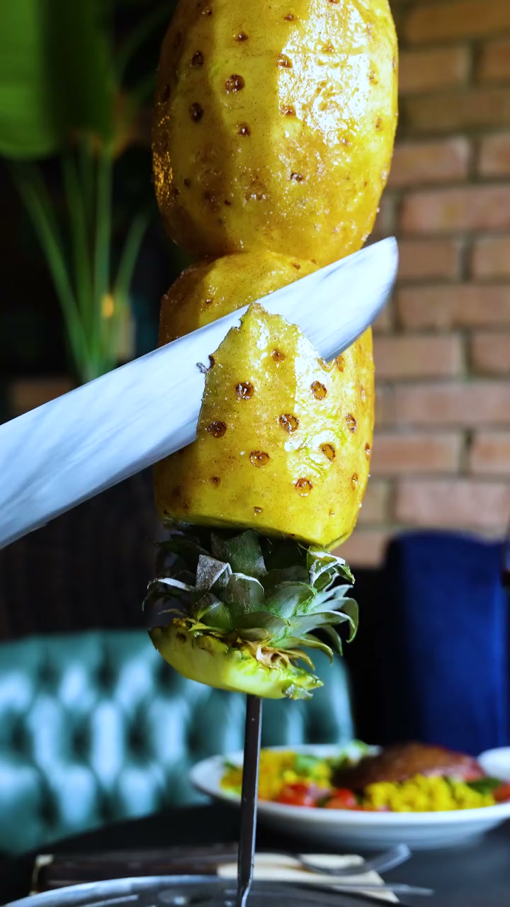 Grilled pineapple being carved from a skewer at the table